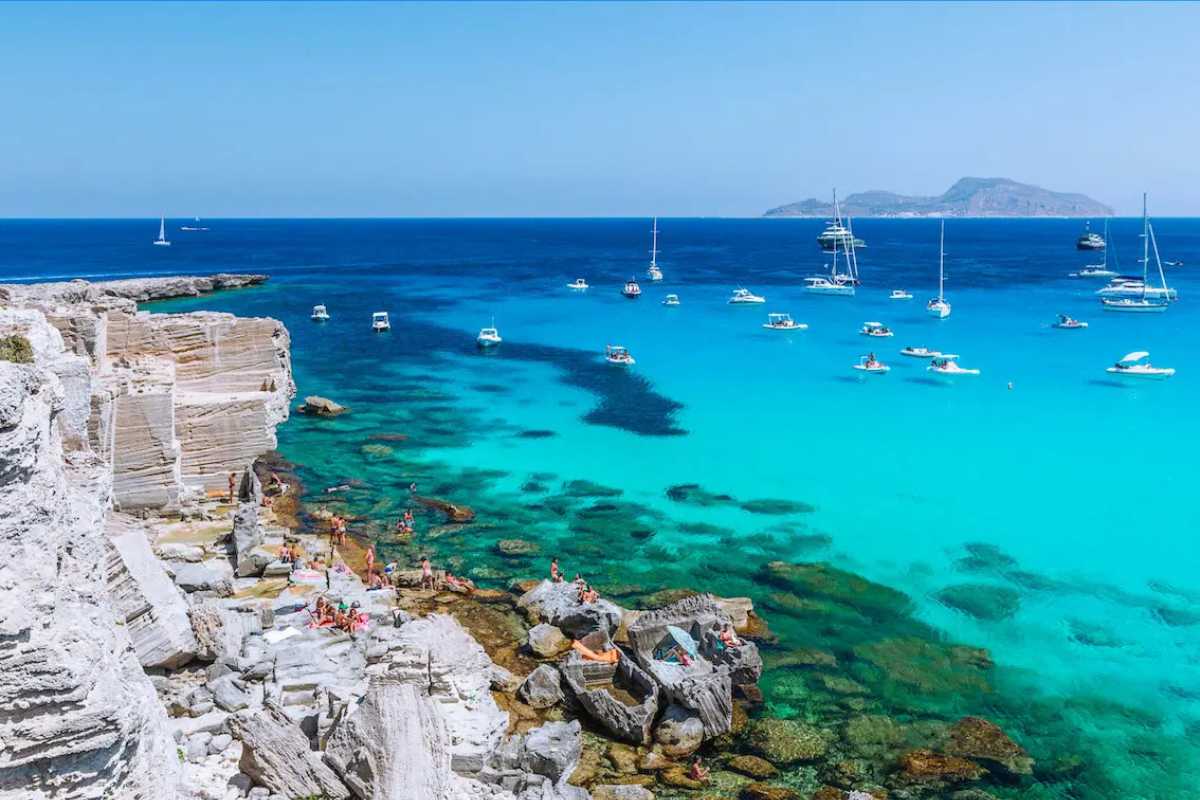 Scena di una festa tradizionale a Favignana, con piazza animata, bandiere colorate, gente locale e turisti che partecipano agli eventi, atmosfera festosa mediterranea